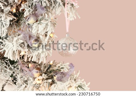 Decoration on Christmas tree - light violet birds and glassy ball on snowy spruce on pink background