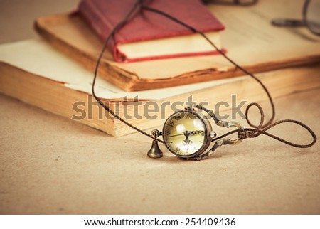 Old-styled pocket or pendant watch with old string and handbell on background of writing-paper and old books