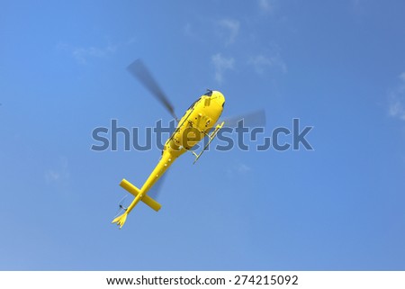 Helicopter rescue, Yellow helicopter in the air while flying on blue sky, bottom view.All logos and text removed.