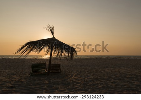 Umbrella and two beach chairs, gold-colored setting sun