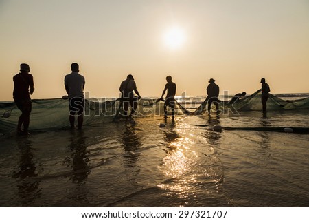 A group of fishermen pulling nets from the sea, in gold-colored sunset
