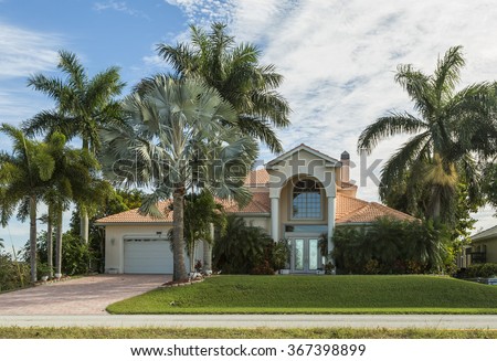 Typical Southwest Florida home in the countryside with palm trees, tropical plants and flowers, grass and pine trees. Inlaid pavement at the entrance. Florida