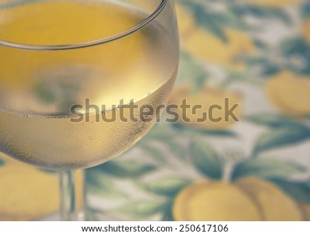 Glass of white wine on yellow pattern table cloth; defocused and vintage filter
