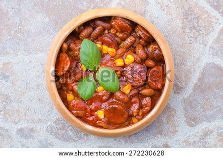 A woody bowl of homemade chili bean goulash with sausage and corn on stone table, soft light