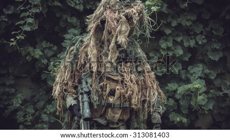 Special soldier in camouflaged sniper suit before action. Photo edited into warfare look and dark atmosphere. Selective focus.