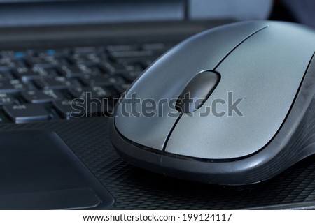 Silver mouse on black laptop. It\'s a working equipment in present.