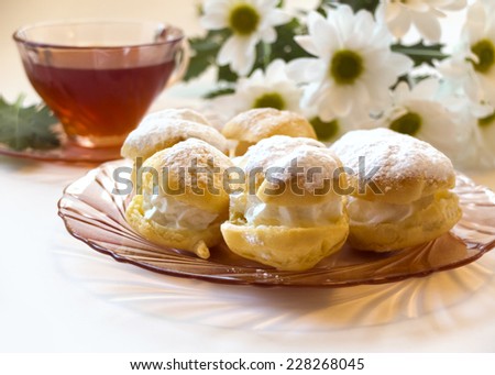 Cream puff or profiterole with filling, powdered sugar topping, chamomile flowers and tea