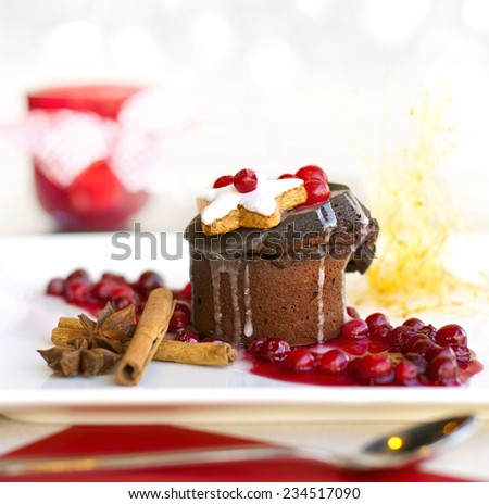 Molten lava cake dessert or dark chocolate souffle served with gingerbread, berries cinnamon sticks, anise on white plate near red candlestick with ribbon