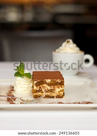 Tiramisu cake - delicious dessert served with whipped cream and a cup of cappuccino
