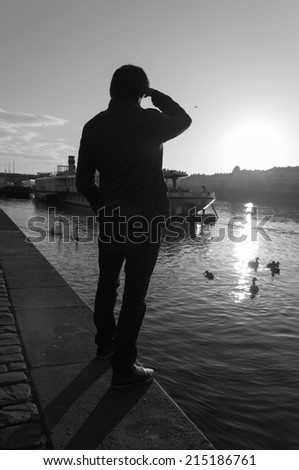 Young man on riverside is looking towards sun in Prague, Czech Republic. B&W image