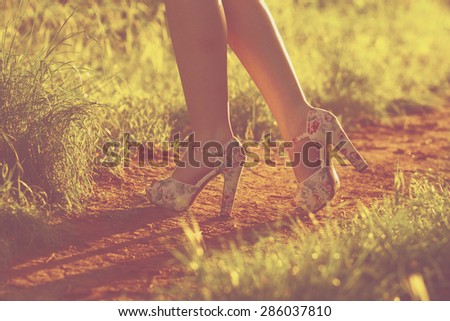 Young female legs walking towards the sunset on a dirt road. Instagram. shoes and woman legs.