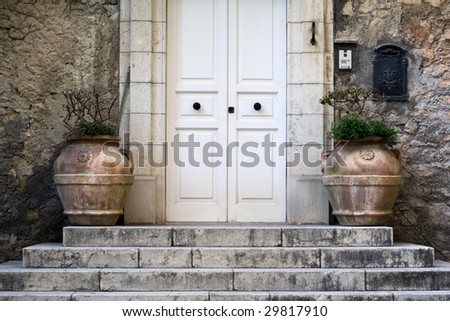 A white door on ancient stairs decorated with two vases on a textured stone wall