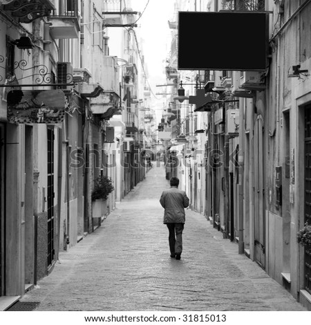 A lonely man walking along a narrow italian medieval street full of closed shops in an early sunday morning
