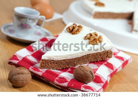 A slice of coffee and walnuts cake laid on a towel, surrounded by the ingredients on a wooden table