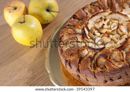 An Apple cake decorated with apple slices on a wooden table with fresh fruit
