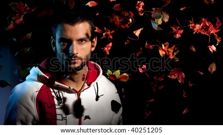 A handsome man under a waterfall of falling red leaves on a black background