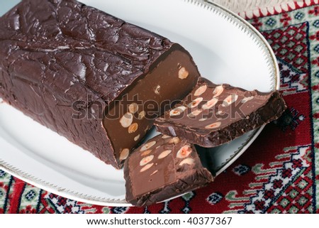An Italian Chocolate Torrone candy block with hazelnuts, dark chocolate and milk chocolate on a white dish over a red rug
