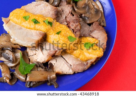 A blue plate on a red background with Chine of Pork in Milk & Carrots Ragu with Champignon Mushrooms