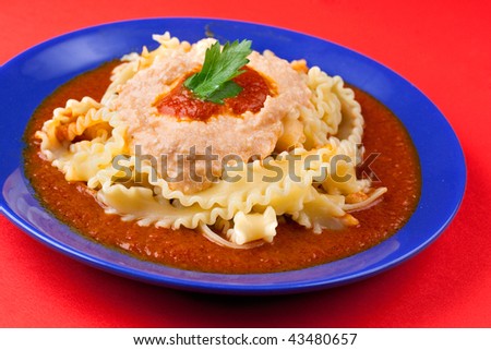 A blue plate on a red background with italian pasta manfredi with ricotta cheese and pork rag? sauce