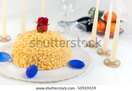 Mimosa cake made of sponge cake, cream pastissarie, whipped cream and orange flavorued. Decorated with small cubes of spongcake all over. Shallow depth of field on rose and cake front
