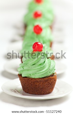 Carrot cupcakes with green whipped cream frosting and a candied cherry on top.