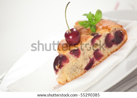 A slice of fresh cherries cake with a fresh cherry on top and a bud of mint. Shallow depth of field on the cherry and the cake\'s tip