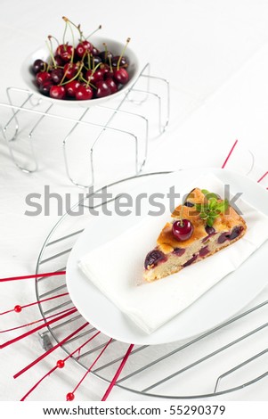 A slice of fresh cherries cake with a fresh cherry on top and a bud of mint. Shallow depth of field on the cherry and the cake\'s tip
