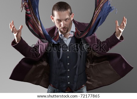 A handsome man standing in front of the camera hit by a strong wind with coat and scarf floating in the air.