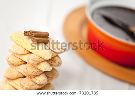 a tower of italian savoiardi cookies with cinnamon sticks on top and a ceramic pot of neapolitan sanguinaccio chocolate sauce in the background