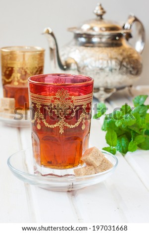 Moroccan tea with mint and sugar in a glass on a white table with a kettle
