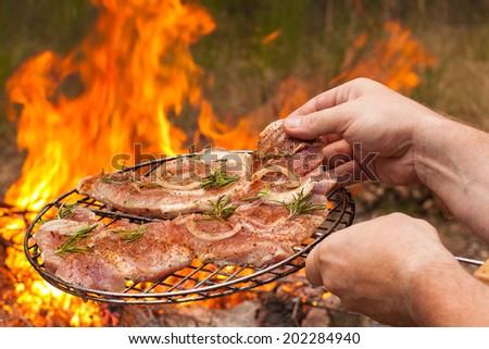 Men's hands hold the grille with meat on fire background