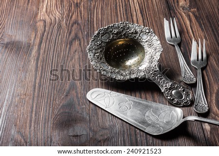 silver cutlery for dessert - strainer for powdered sugar, cake spatula and forks on a wooden background