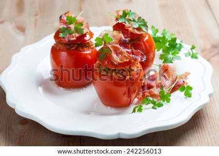 baked tomatoes stuffed with bacon and buckwheat flakes on a white plate on a wooden background