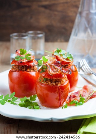 baked tomatoes stuffed with bacon and buckwheat flakes on a white plate on a wooden background