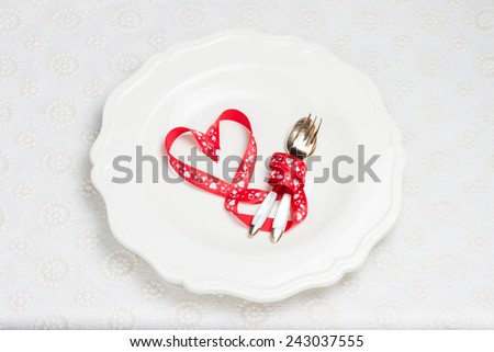 red ribbon in the form of heart on a white plate with cutlery. romantic dinner for two lovers