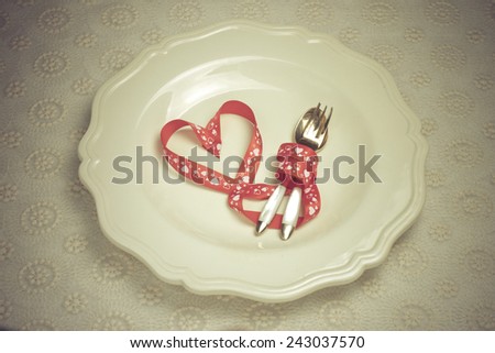 red ribbon in the form of heart on a white plate with cutlery. romantic dinner for two lovers
