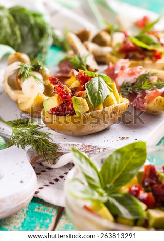 potatoes stuffed with vegetables. Boats potatoes with avocado, sun-dried tomatoes, bacon, cheese, olives, pickled cucumbers and greens on the board on a green wooden background. Picnic, barbecue grill