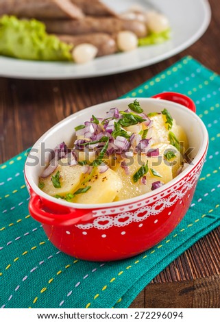 potato salad with red and green onions in a red pot.