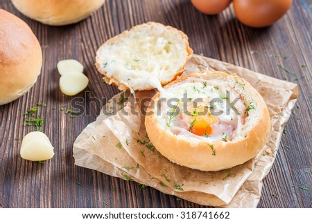 Sandwich with egg, cheese and bacon. Hot breakfast. Bun with liquid egg, bacon and melted cheese on dark wooden background