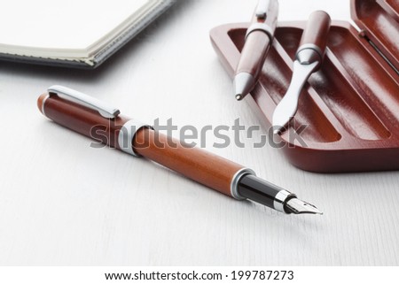 Wooden fountain pen and roller pen with leather notebook on white background.