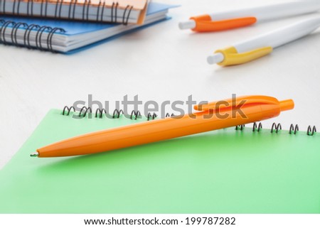 Orange plastic ball pen with green notebook at the back office supplies on white background.