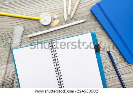 Office supply collection - sharpener, pencils, ball pen, notebooks and ruler - on brown wooden table.