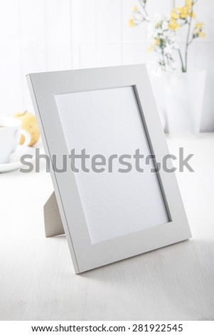 blank white picture frame with yellow flowers, coffee cup and apple on white desk