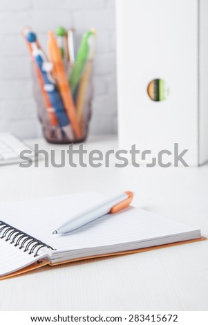 orange ball pen with notebook with multicolored ball pens and folders on white desk