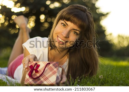 Young cute  Caucasian woman wondering what is in the red gift box looking sideways making facial expression