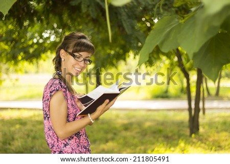 Girl with glasses reading a book in the park. Student studying in park Joyful happy European girl student sitting writing and reading outside on university campus or park.