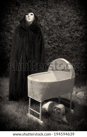 Vintage looking photo of a creepy masked and cloaked person standing next to an eerie, empty baby crib.