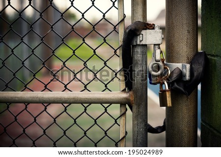 Closeup of a locked padlock securing a metal chain-link gate.