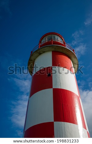 Unusual perspective image of a towering red and white lighthouse standing against a rich, deep blue sky.