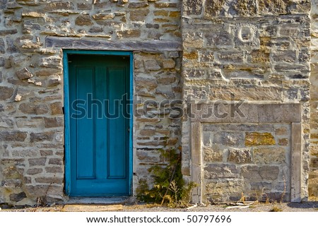A blue door in a stone wall with stoned-up fireplace like structure.